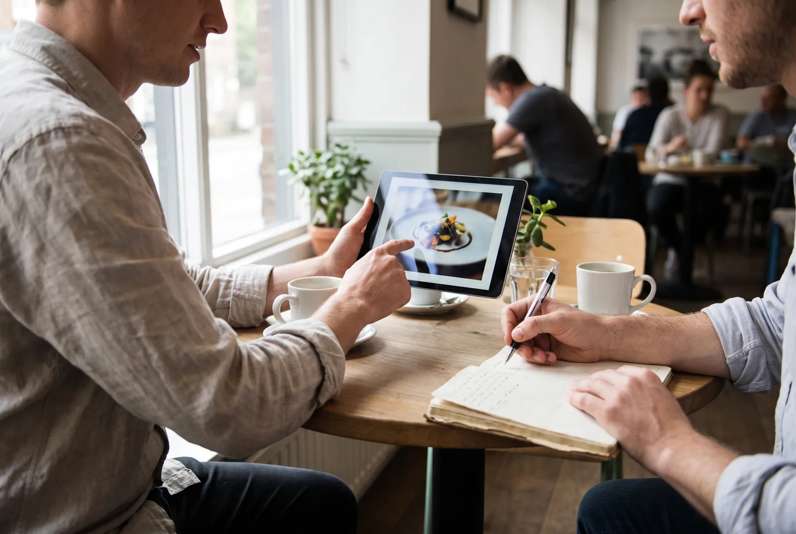 A client points at a post preview on a tablet while their social media manager notes the change, the kind of feedback that belongs in one place.